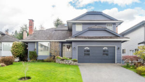 Exterior of a blue multi-story home with a wide concrete driveway, green lawn, and attached two-car garage under a cloudy sky.